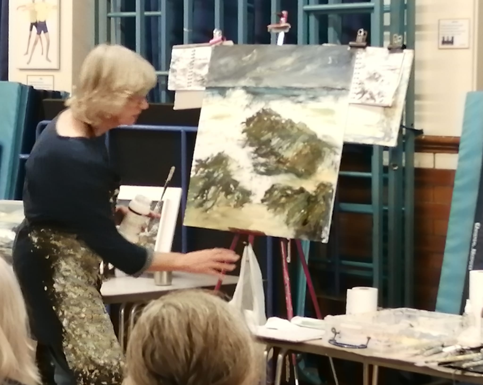 A person talking to a group with paintings in the background